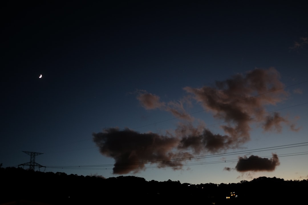 Crescent moon in a dark twilight sky with clouds.